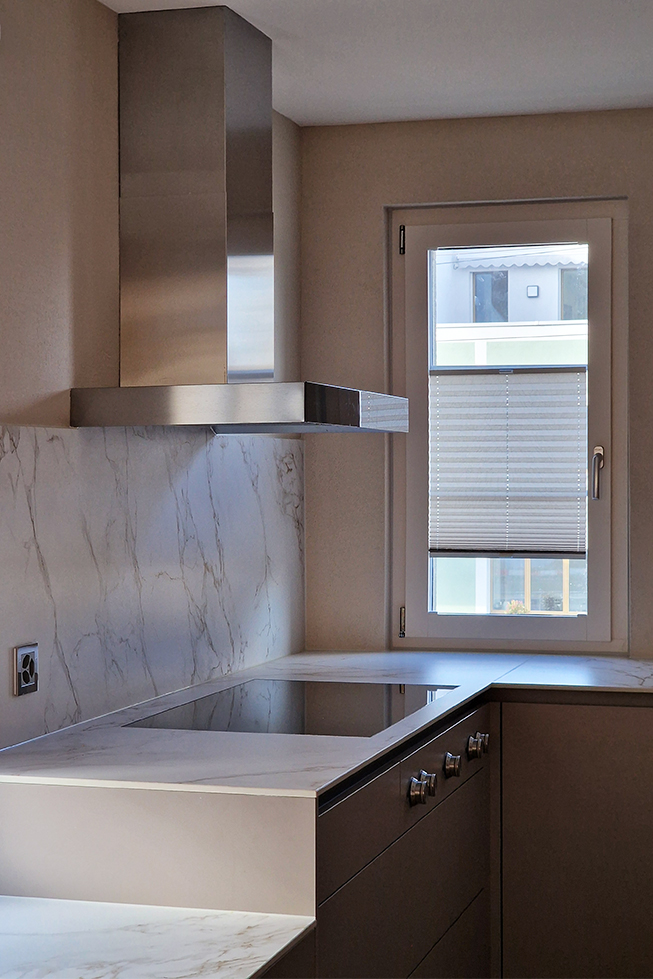 Fenster mit Blick auf die Strasse, grau-beige Küche, Arbeitsfläche aus Stein, Gaggenau-Herd, Steckdose mit Metallrahmen