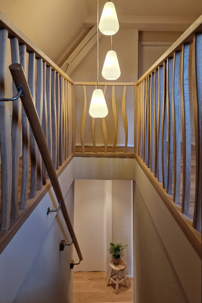 Vorhandener Holzbalken, hängende Lampen, sanftes Licht, Design-Geländer, Hocker mit Zimmerpflanze