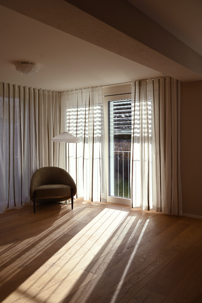 Hausanbau, Deckenbalken, ein Sessel mit einer Stehlampe, Vorhänge mit Linien, helle Schatten auf dem Boden